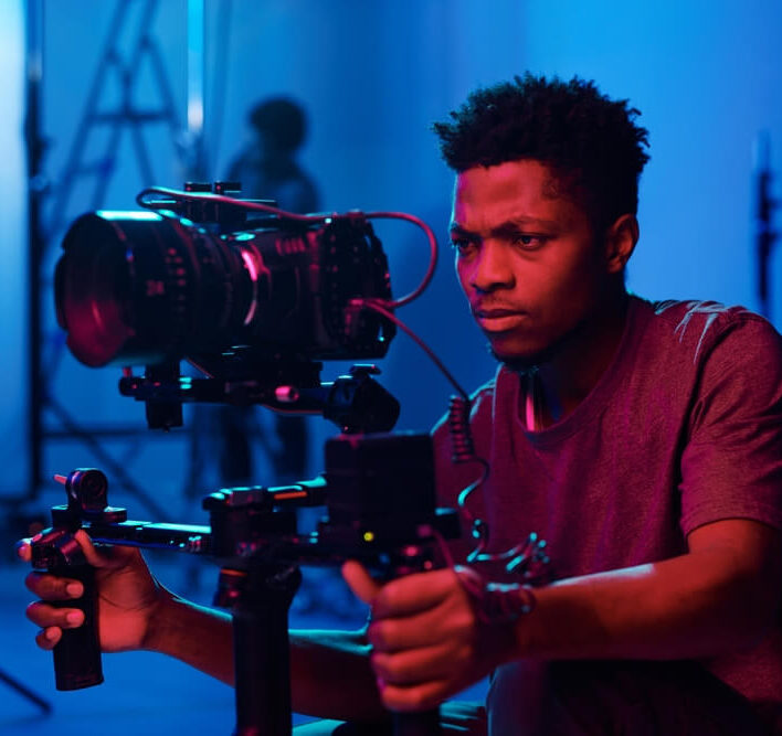 Cinematographer operating a professional camera rig on a film set with pink and blue lighting.